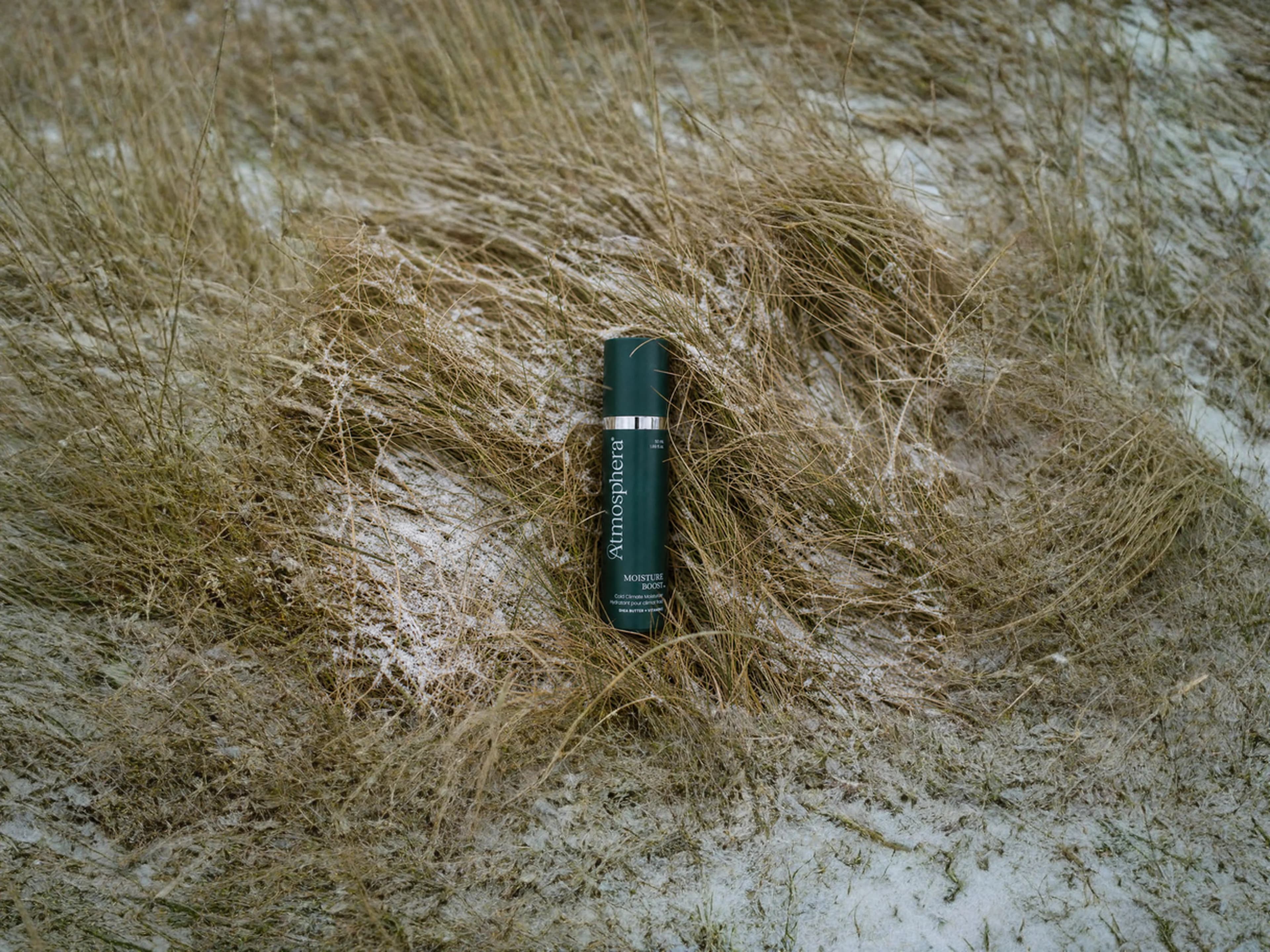 Moisture Boost bottle resting in dry grass dusted with snow