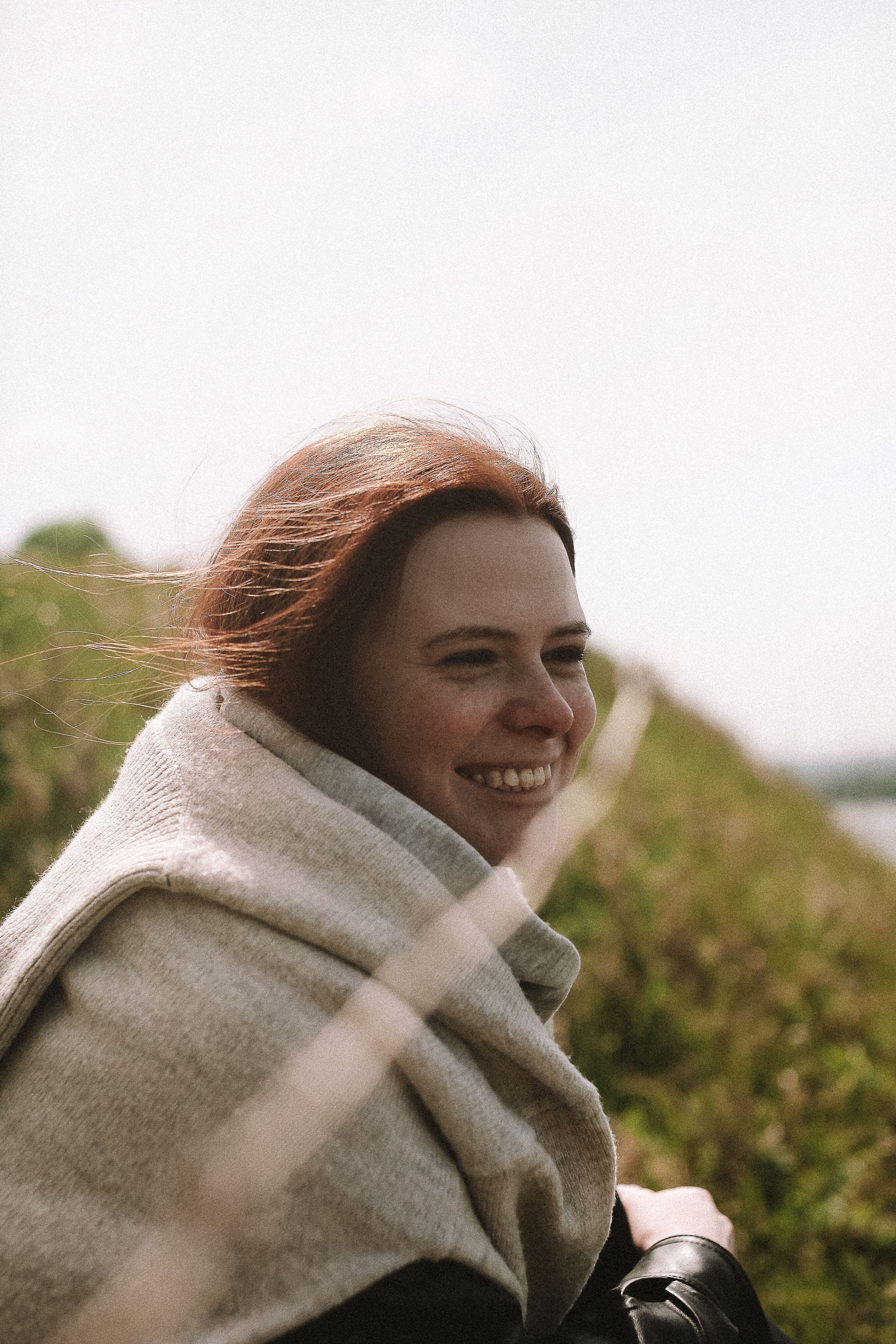 Smiling woman wrapped in a knit sweater outdoors on a windy day